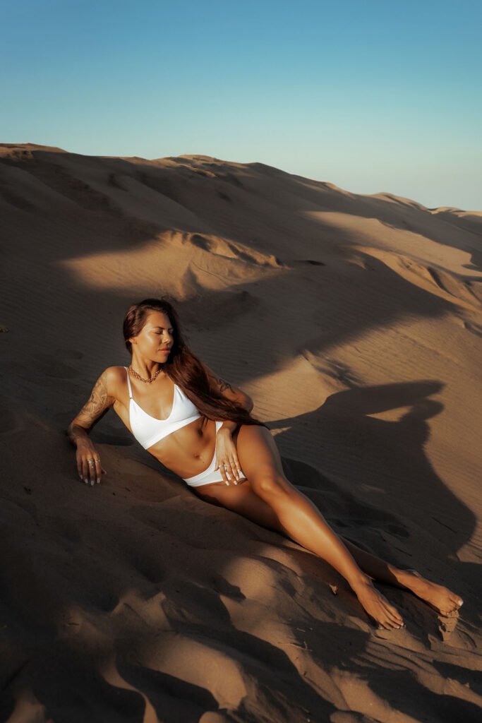 Woman posing in a white bikini on sand dunes under the bright sun, showcasing the expertise of a photographer in Marbella.